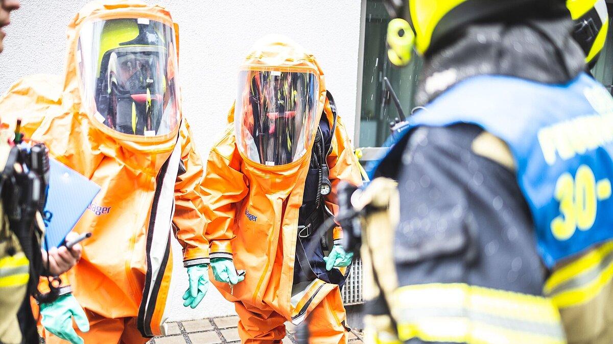 2 Feuerwehrmänner in orangenen Schutzanzügen. © Amt für Brand- und Katastrophenschutz