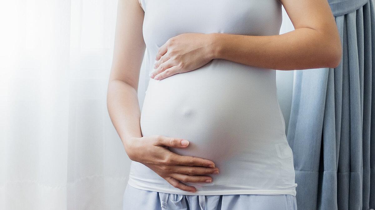 eine Schwangere hält ihren Bauch sanft mit beiden Händen . © stock.adobe.com / Nattakorn