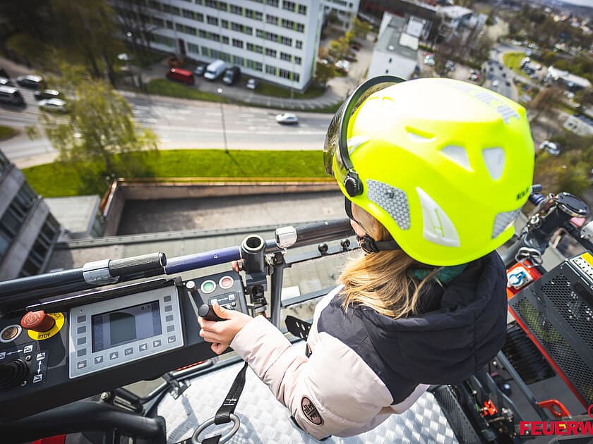 Junges Mädchen steht auf der Drehleiter der Feuerwehr mit einem Helm auf dem Kopf. © Stadt Gera