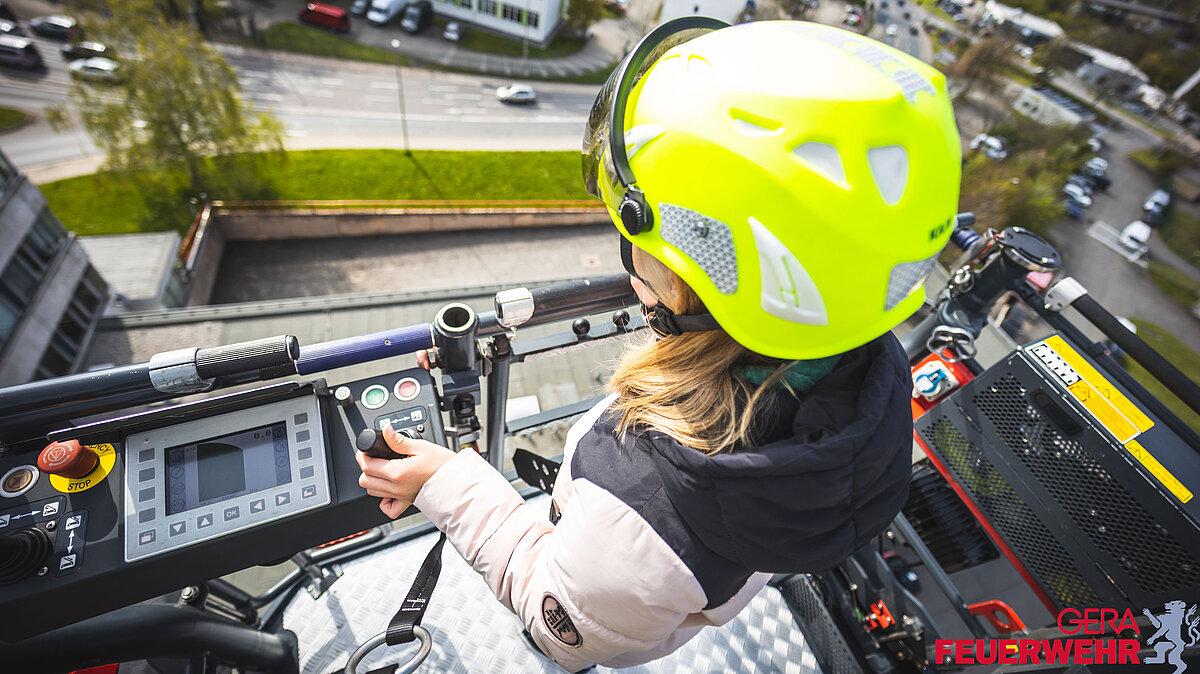 Junges Mädchen steht auf der Drehleiter der Feuerwehr mit einem Helm auf dem Kopf