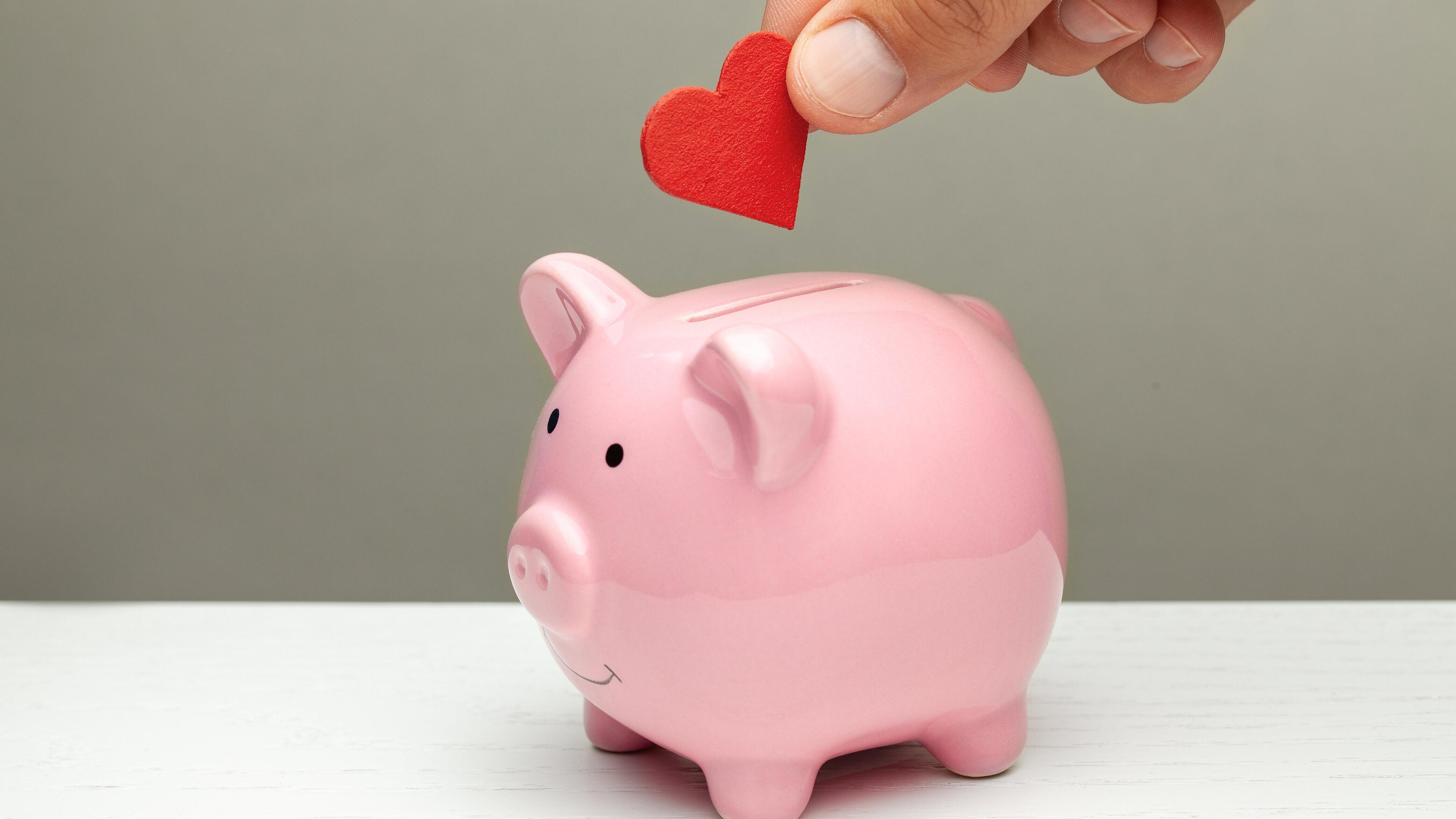 ein Stoffherz wird in ein Sparschwein gesteckt. © stock.adobe.com