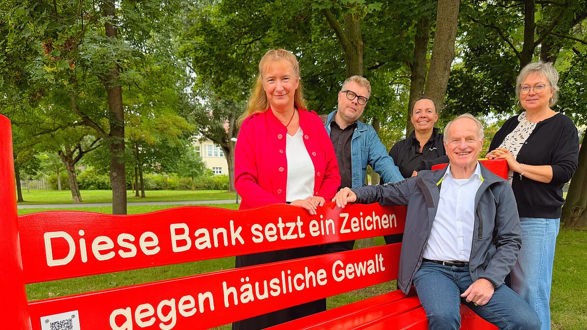 rote Bank, daneben stehen zwei Männer und 3 Frauen. © OTEGAU/SN