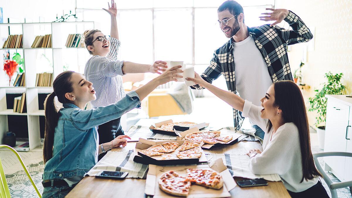 Vier junge Menschen essen gemeinsam Pizza in einer Wohngemeinschaft. 