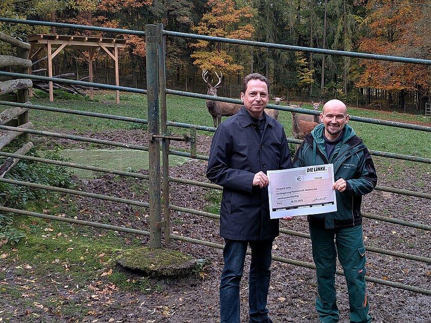 Herr Schubert und Herr Horn stehen vor dem Gehege der Rothirsche, welche im Hintergrund zu sehen sind. © Die Linke