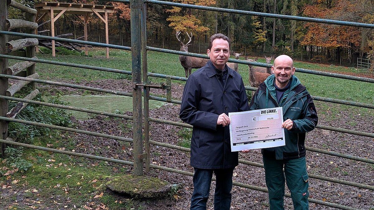 Herr Schubert und Herr Horn stehen vor dem Gehege der Rothirsche, welche im Hintergrund zu sehen sind. © Die Linke