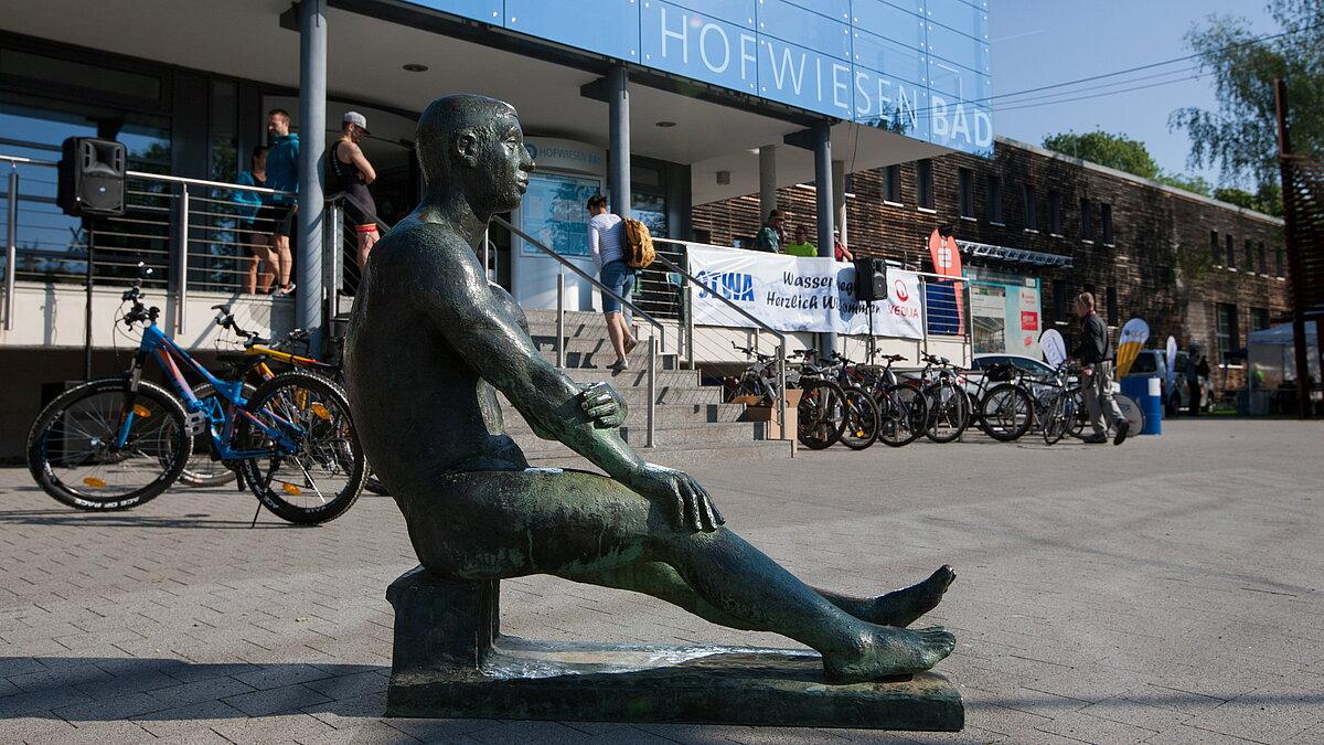 Eine Bronze-Skulptur in Form eines sitzenden Mannes vor dem Eingang eines Gebäudes. © Steffen Weiss