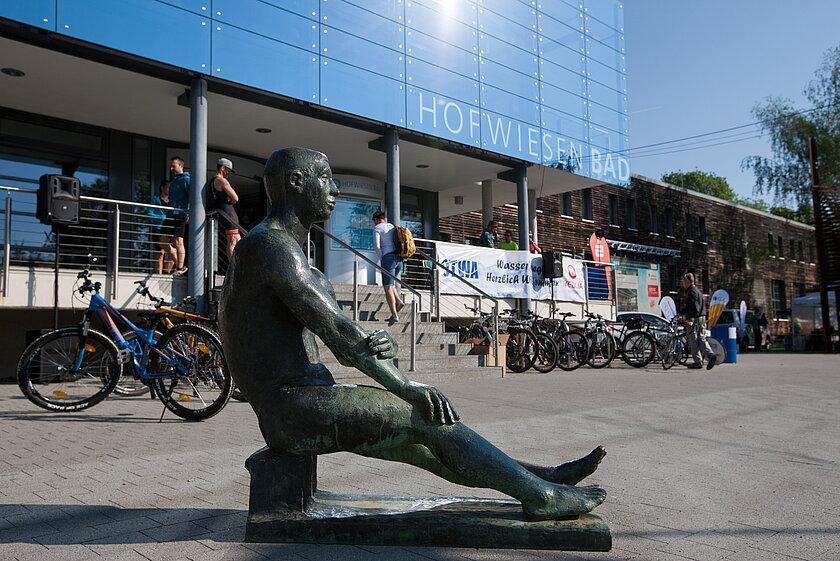 Eine Bronze-Skulptur in Form eines sitzenden Mannes vor dem Eingang eines Gebäudes. © Steffen Weiss