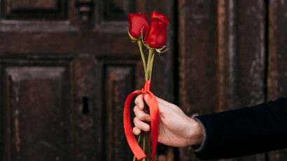 Eine Herrenhand hält zwei rote Rosen mit einer roten Schleife. © freepik.com
