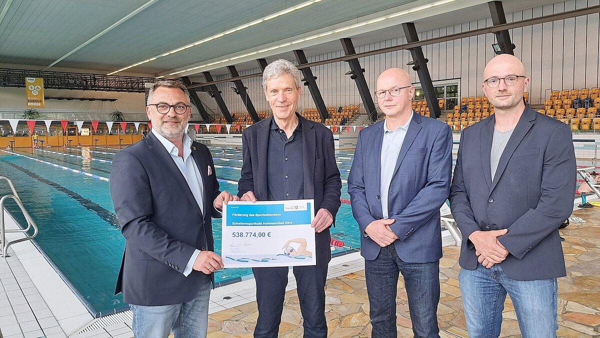 Minister Helmut Holter übergibt den Fördermittelbescheid an Oberbürgermeister Julian Vonarb vor dem großen Schwimmbecken im Hofwiesenbad. © Stadt Gera
