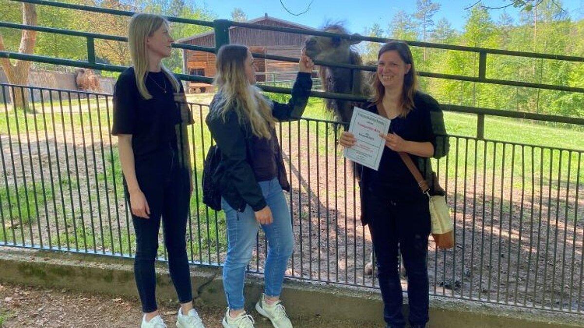 drei Frauen stehen vor einem Trampeltiergehege und besiegeln die Patenschaft für ein Trampeltier. © Stadt Gera