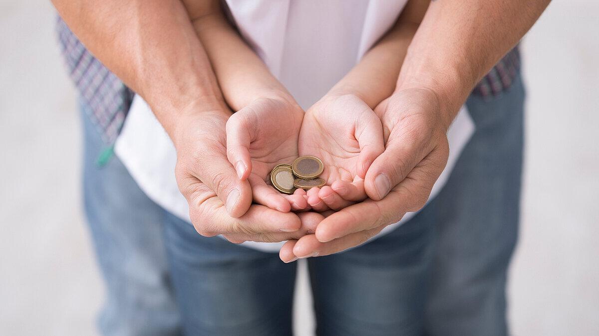 Kinderhände liegen in Erwachsenenhänden, darin liegen Münzen. © Adobe Stock
