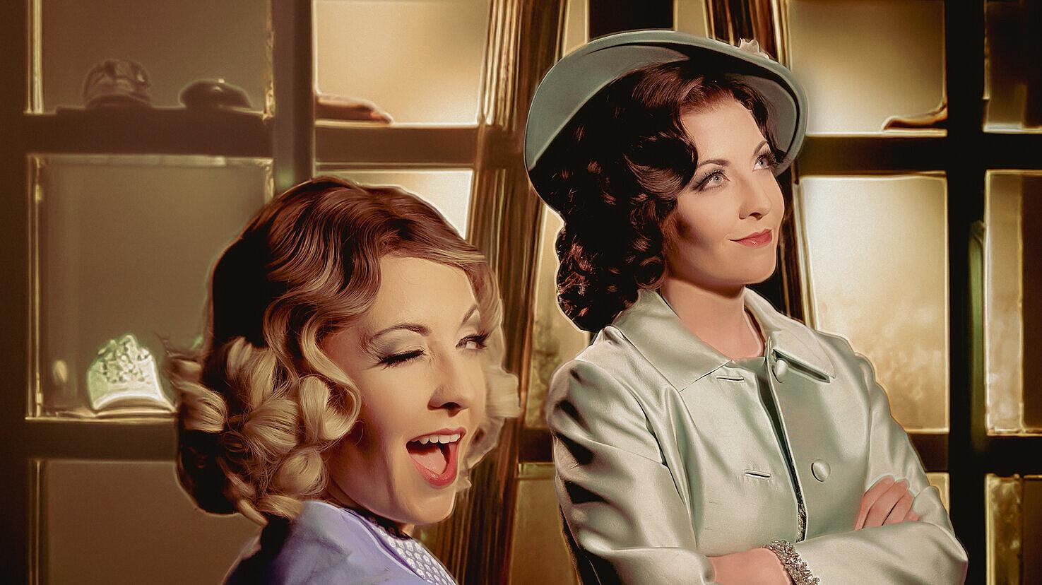 Zwei weibliche Schauspielerinnen während einer Aufführung - eine lächelt und blinzelt in die Kamera. © Theater Gera Altenburg