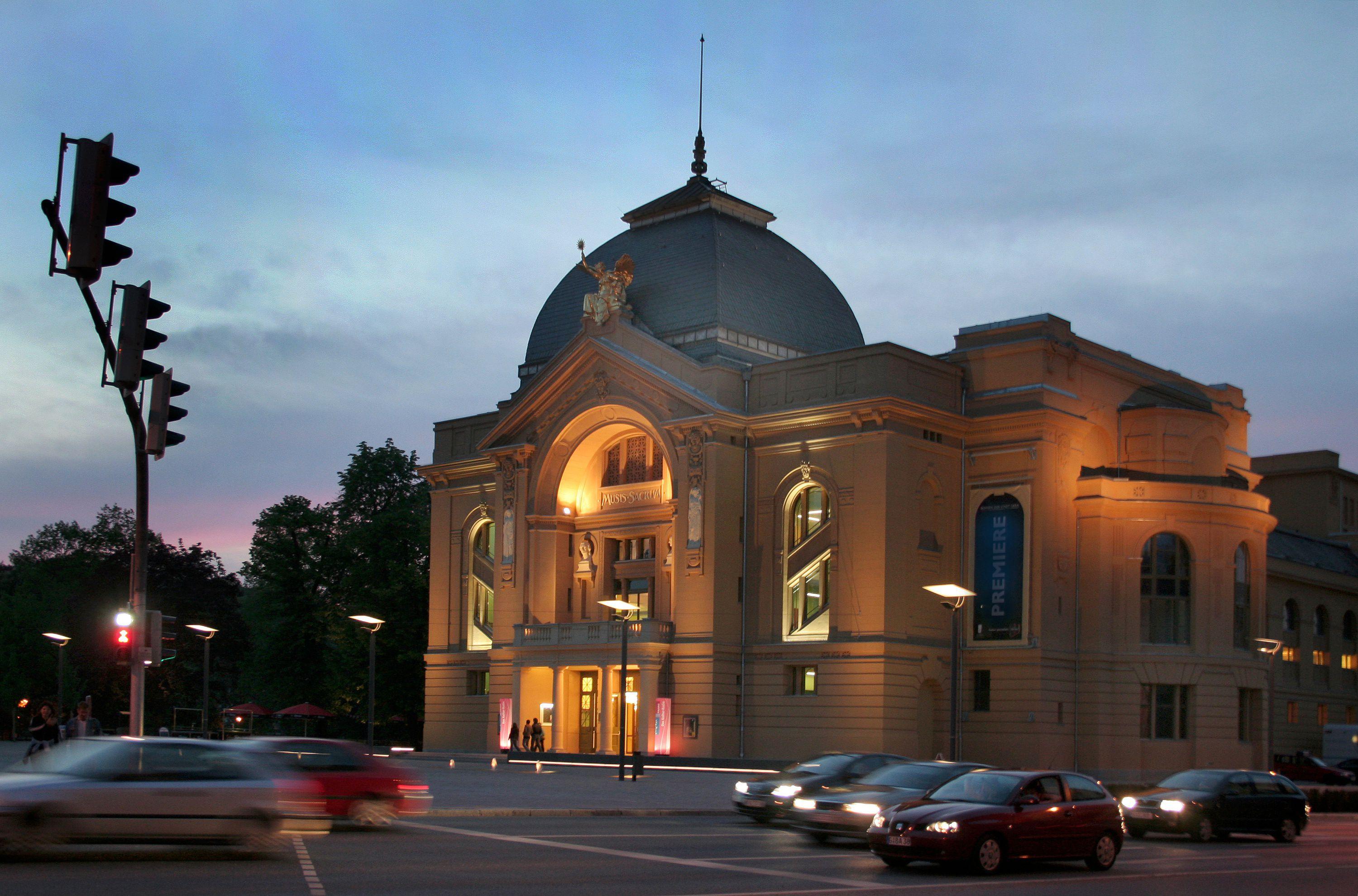 Das Theater, beleuchtet, davor die Straße mit Autos