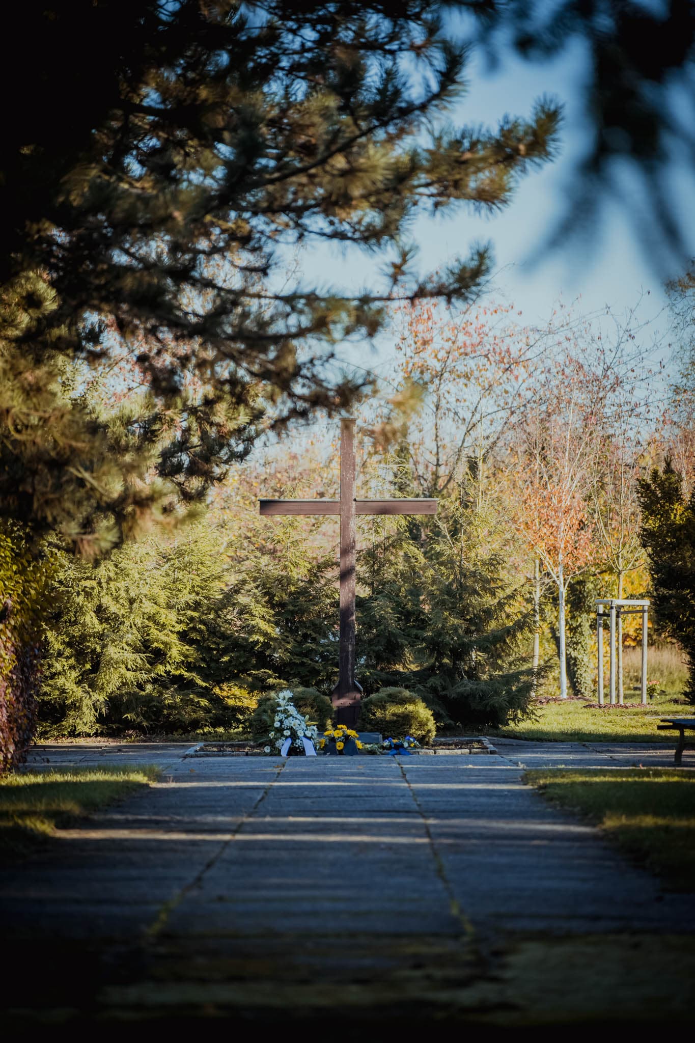 großes Holzkreuz, davor Blumenkränze