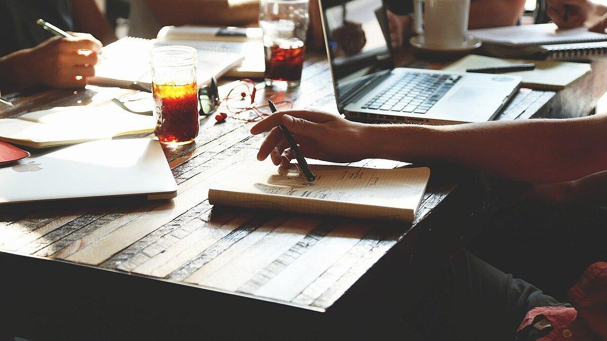 Mehrere Menschen sitzen mit Notizheften an einem Tisch. © Pixabay