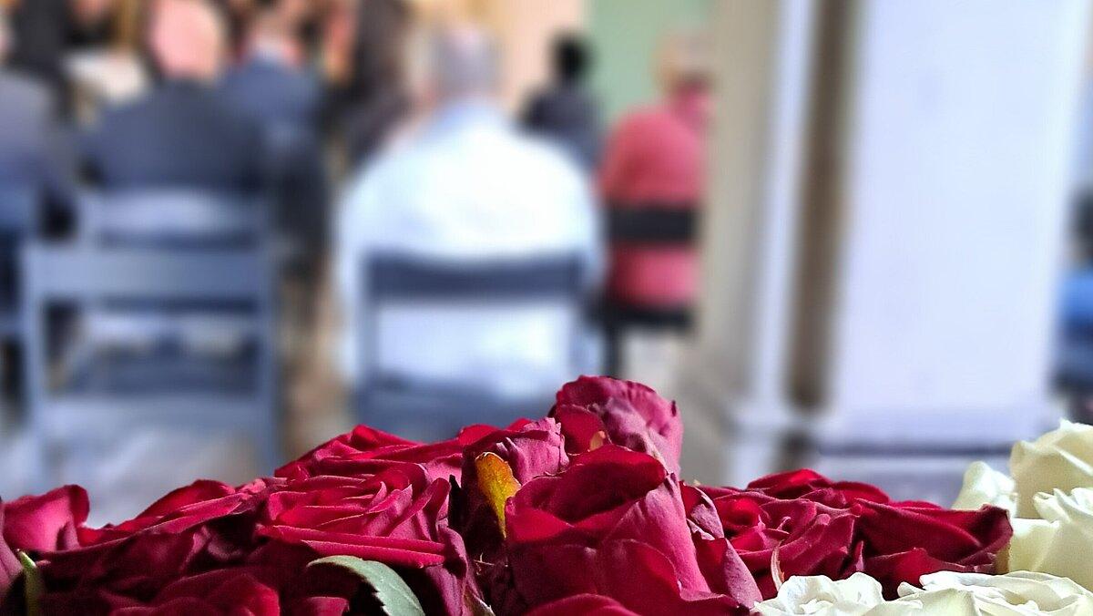 Im Hintergrund mehrere Menschen, die an einer Gedenkfeier teilnehmen, vorn rote und weiße Rosen. © Stadt Gera