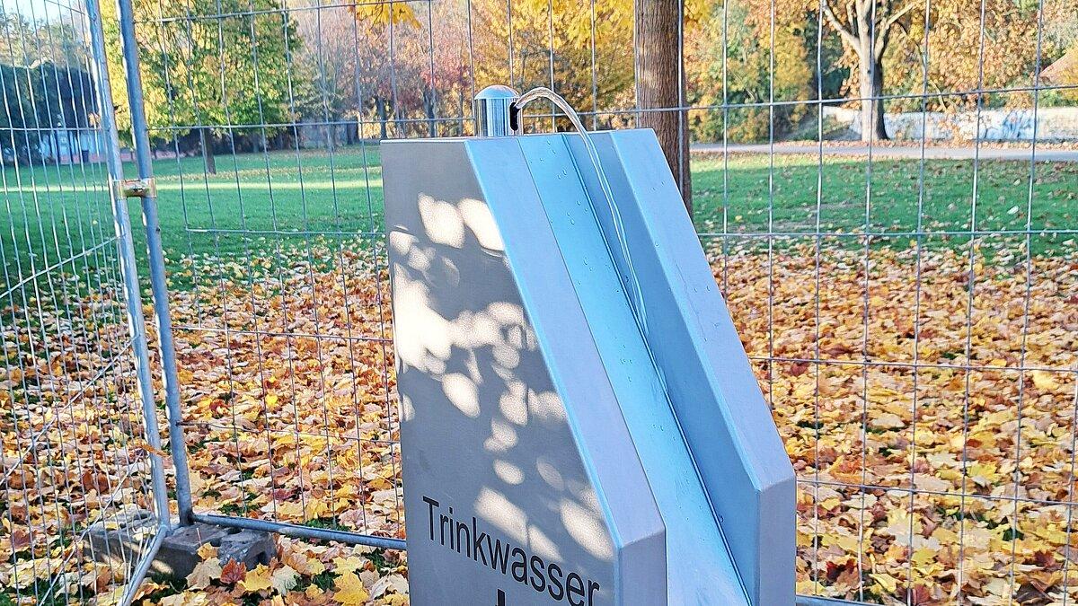 Ein silberner Trinkbrunnen, aus dem ein Wasserstrahl kommt; im Hintergrund Baume und Wiese. © Stadt Gera