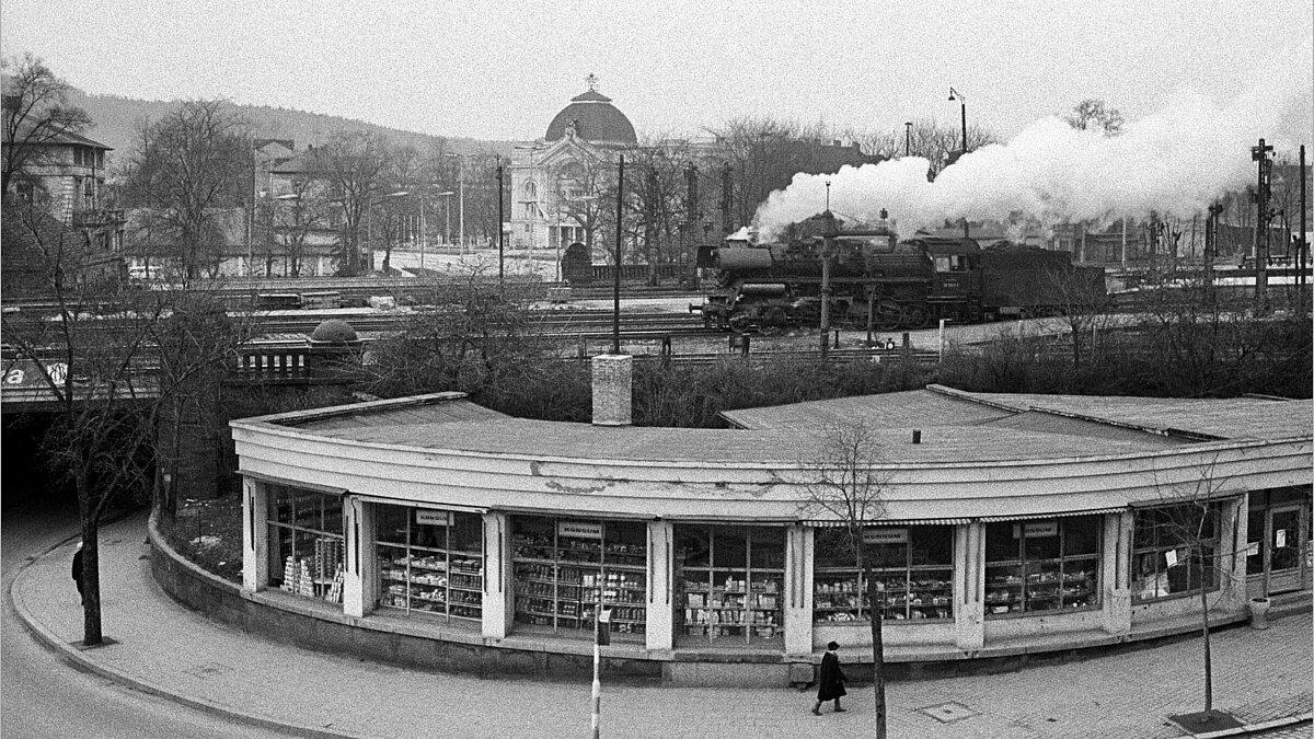 Großfoto des Rundkonsums in der Bahnhofstraße 1975, im Hintergrund die Bahnstrecke mit einer vorbeifahrenden Lok und das Theater