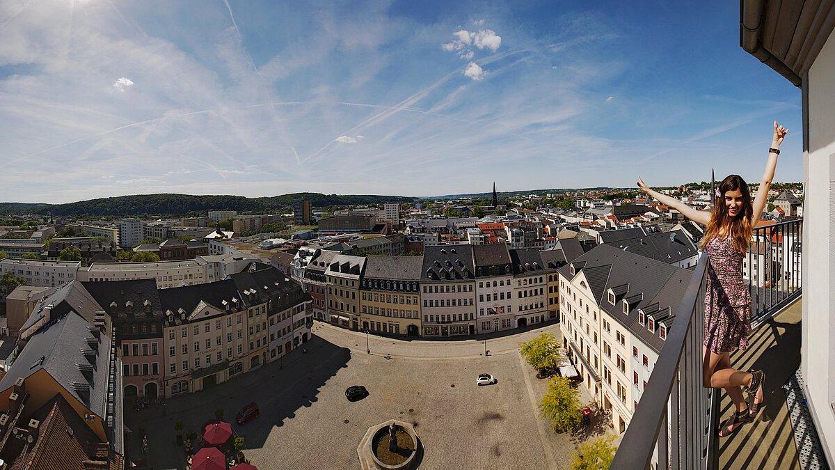 Eine Frau steht auf dem Rathausturm. Neben ihr ist der Geraer Marktplatz und Teile der Innenstadt zu sehen. 