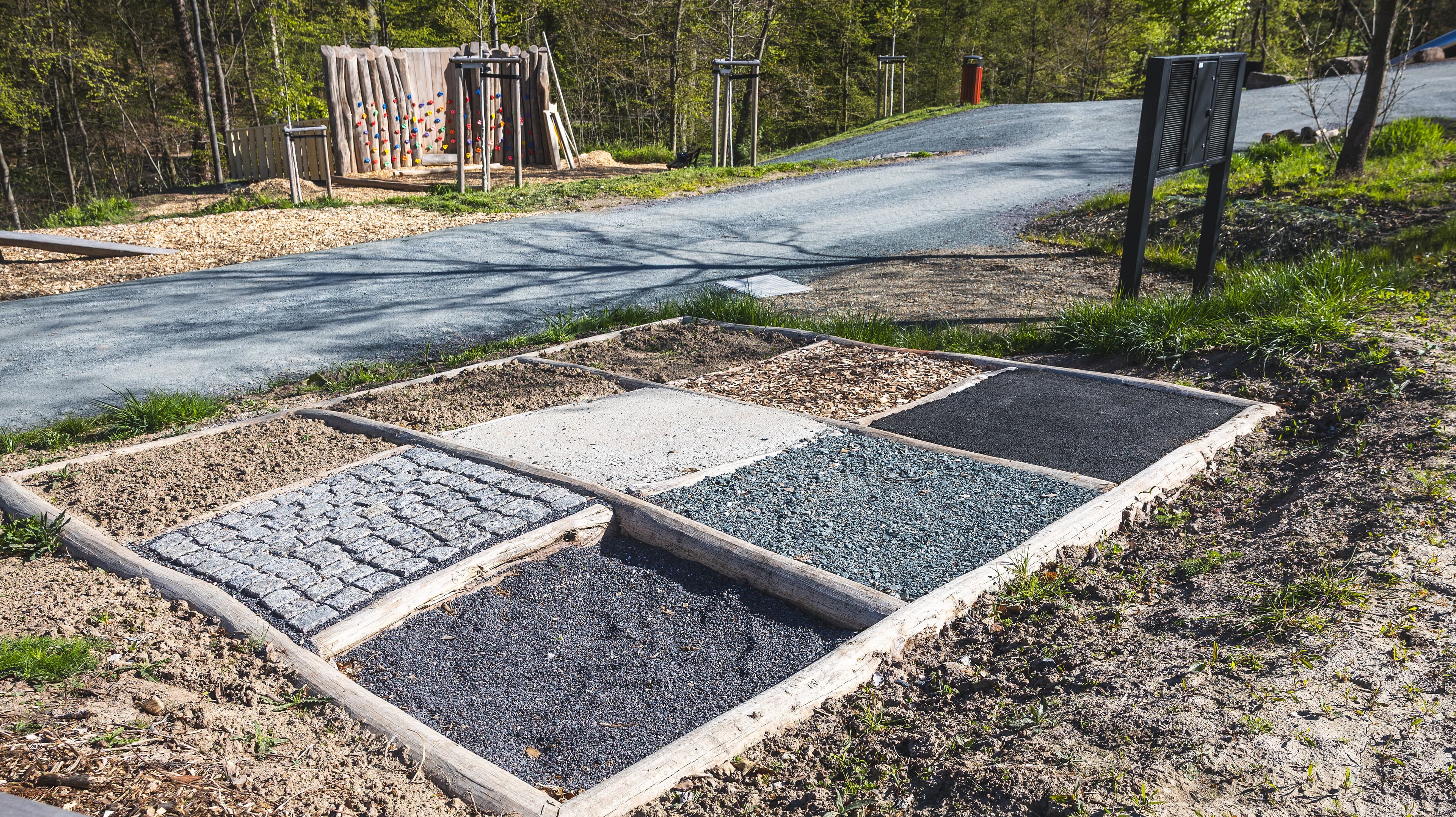 Eine Fläche mit verschiedenen Bodenbelägen umgeben von Rindenmulch und Grün. © Stadt Gera