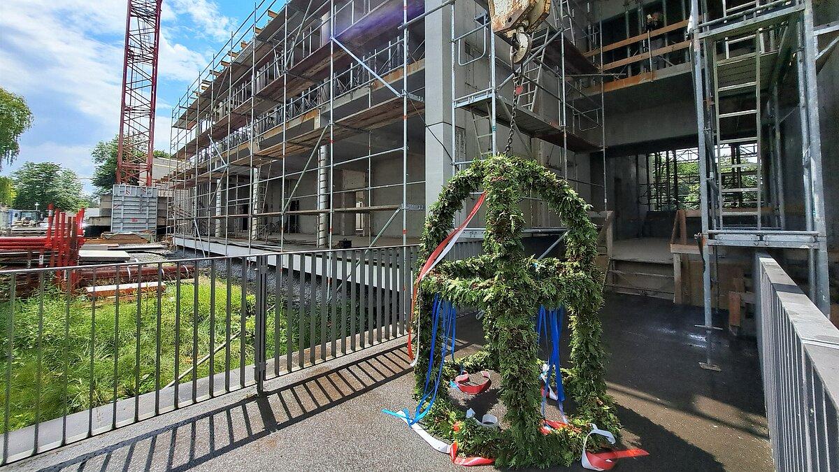 Eine Baustelle für ein Gebäude, vor dem ein Kran mit Richtkranz steht. © Stadt Gera