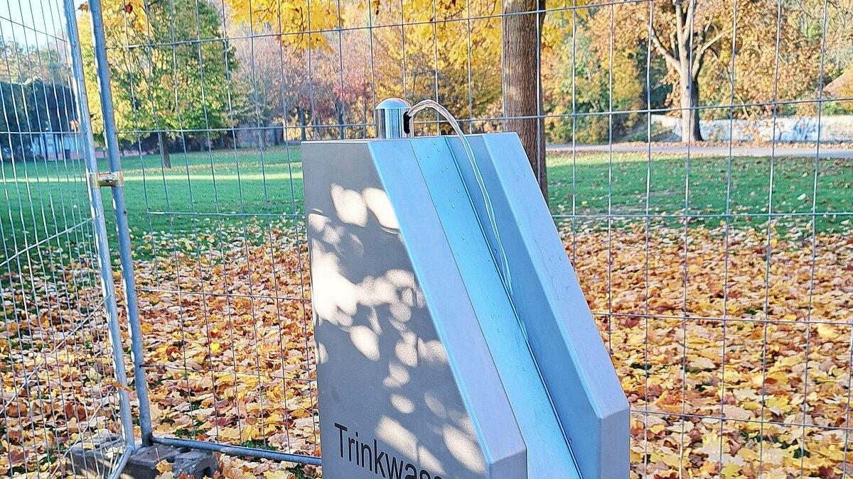 Ein silberner Trinkbrunnen, aus dem ein Wasserstrahl kommt; im Hintergrund Baume und Wiese. © Stadt Gera
