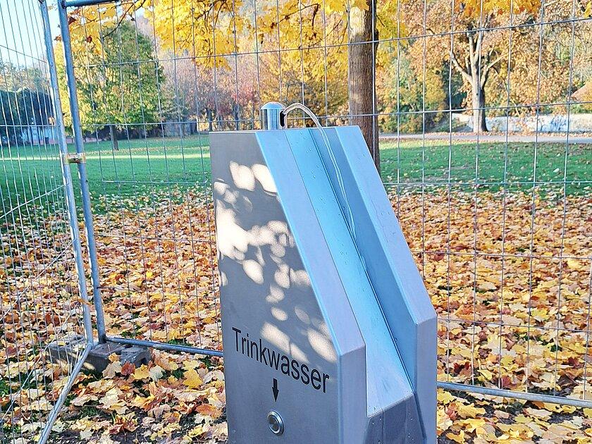 Ein silberner Trinkbrunnen, aus dem ein Wasserstrahl kommt; im Hintergrund Baume und Wiese. © Stadt Gera