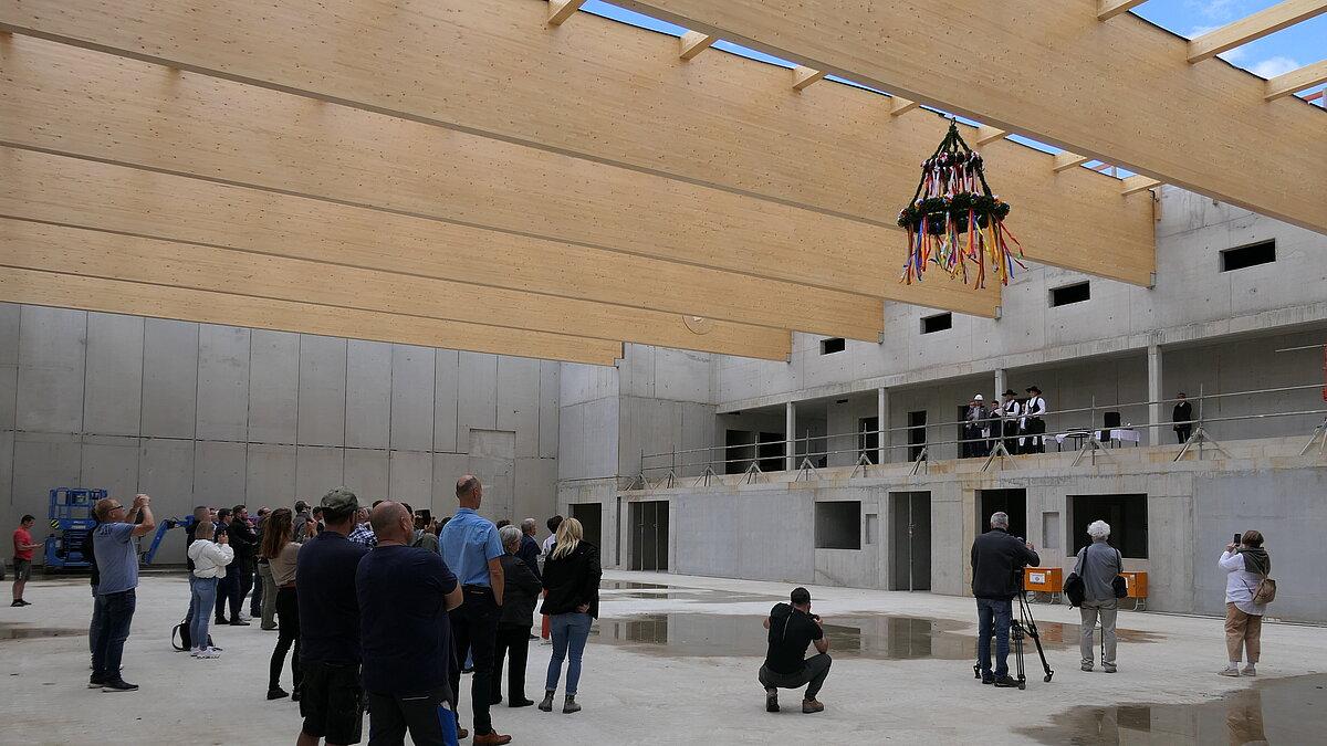 Mehrere dutzend Menschen, die im Rohbau einer Sporthalle stehen und die dem Richtspruch zu Richtfest lauschen. © Stadt Gera