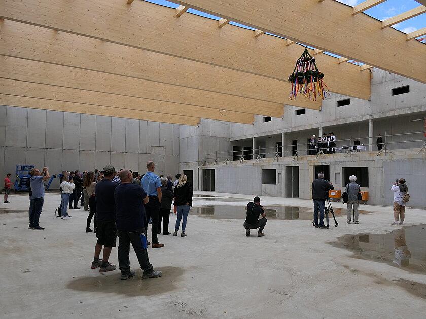Mehrere dutzend Menschen, die im Rohbau einer Sporthalle stehen und die dem Richtspruch zu Richtfest lauschen. © Stadt Gera