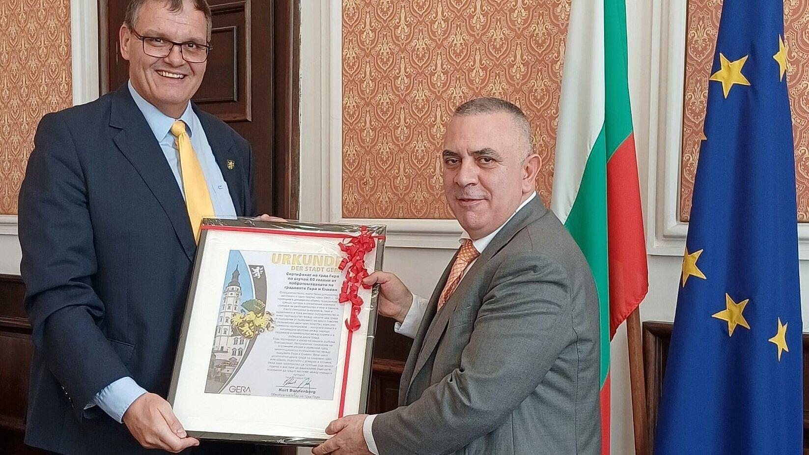 die beiden Männer stehen einander gegenüber und halten die gerahmte Urkunde in den Händen. © Stadt Gera