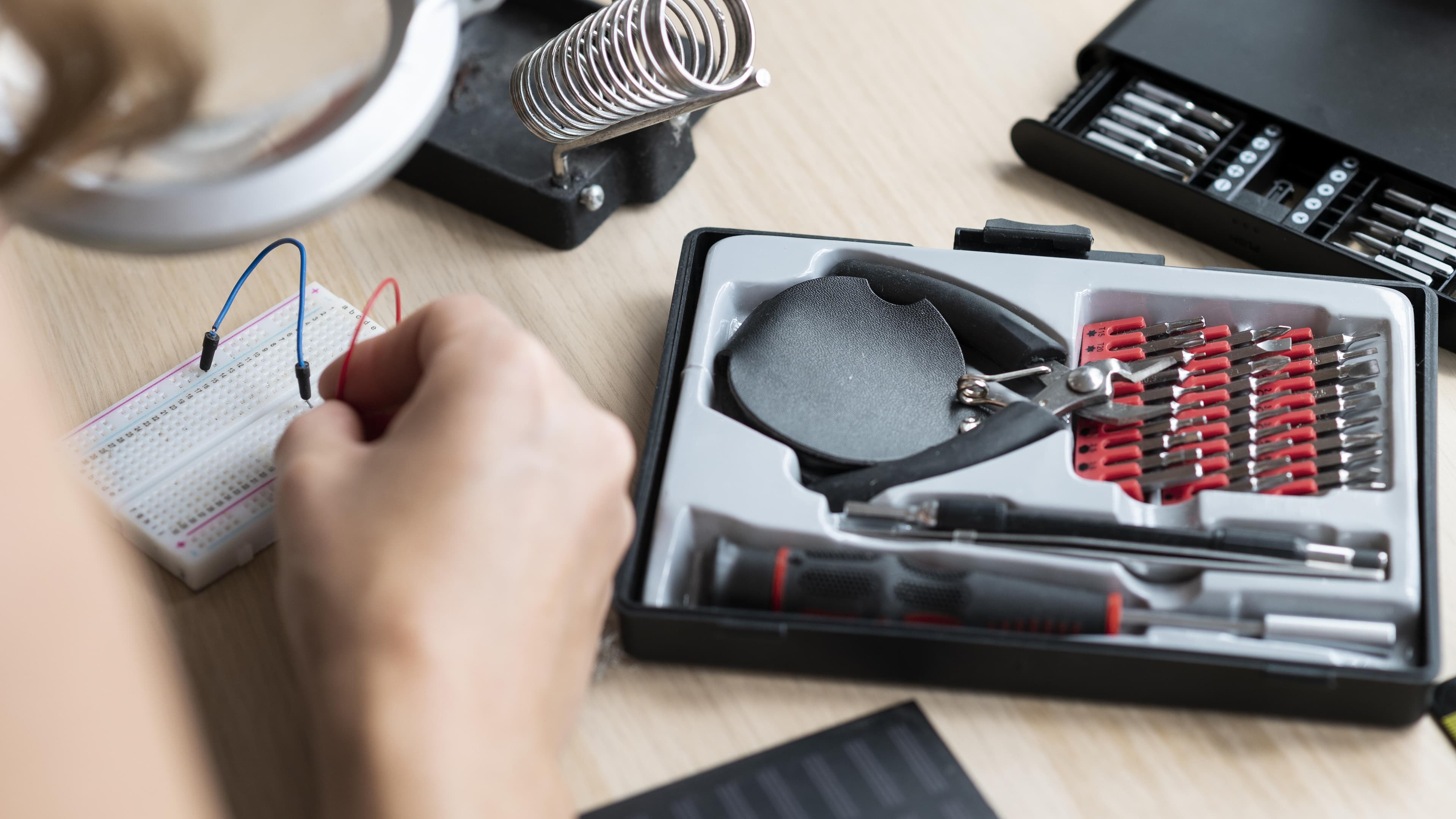 Eine Person lötet auf einer Platine. Im Hintergrund stehen hierzu das passende Werkzeug bereit.. © Freepik