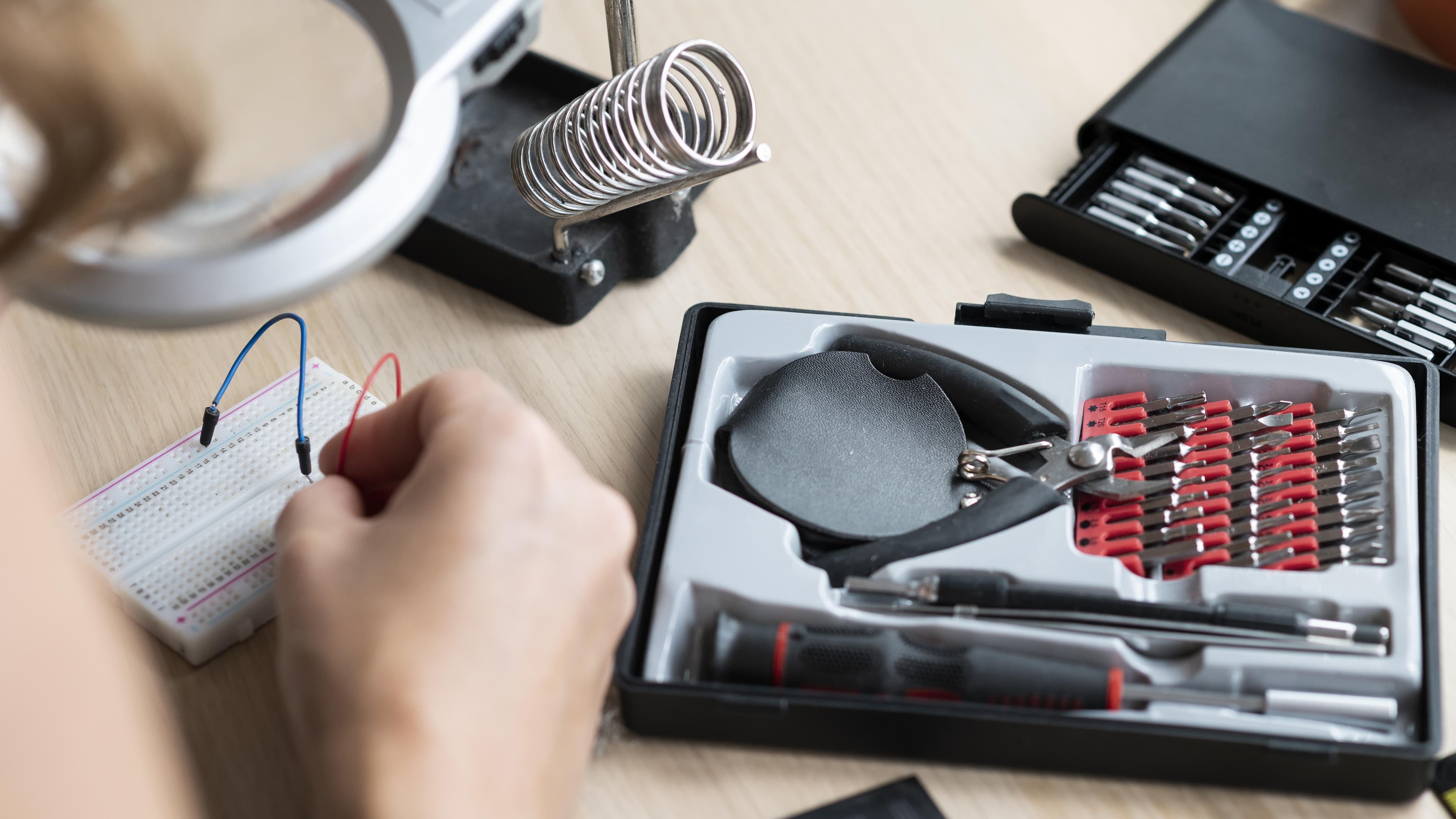 Eine Person lötet auf einer Platine. Im Hintergrund stehen hierzu das passende Werkzeug bereit.. © Freepik