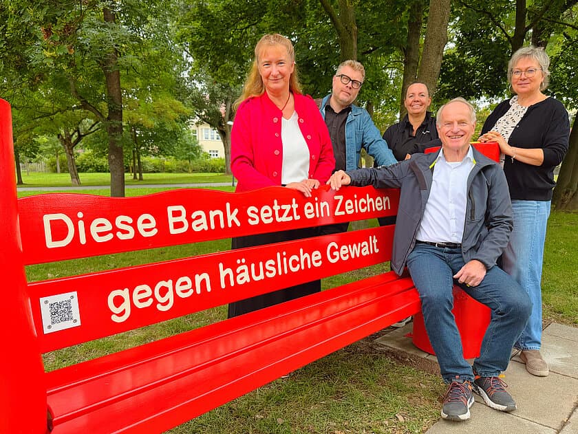 rote Bank, daneben stehen zwei Männer und 3 Frauen. © OTEGAU/SN