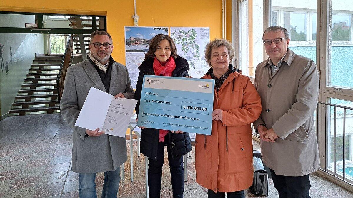 Vier Menschen in einem alten Schulgebäude, im Hintergrund Bilder, wie die Schule nach der Renovierung aussehen soll. © Stadt Gera