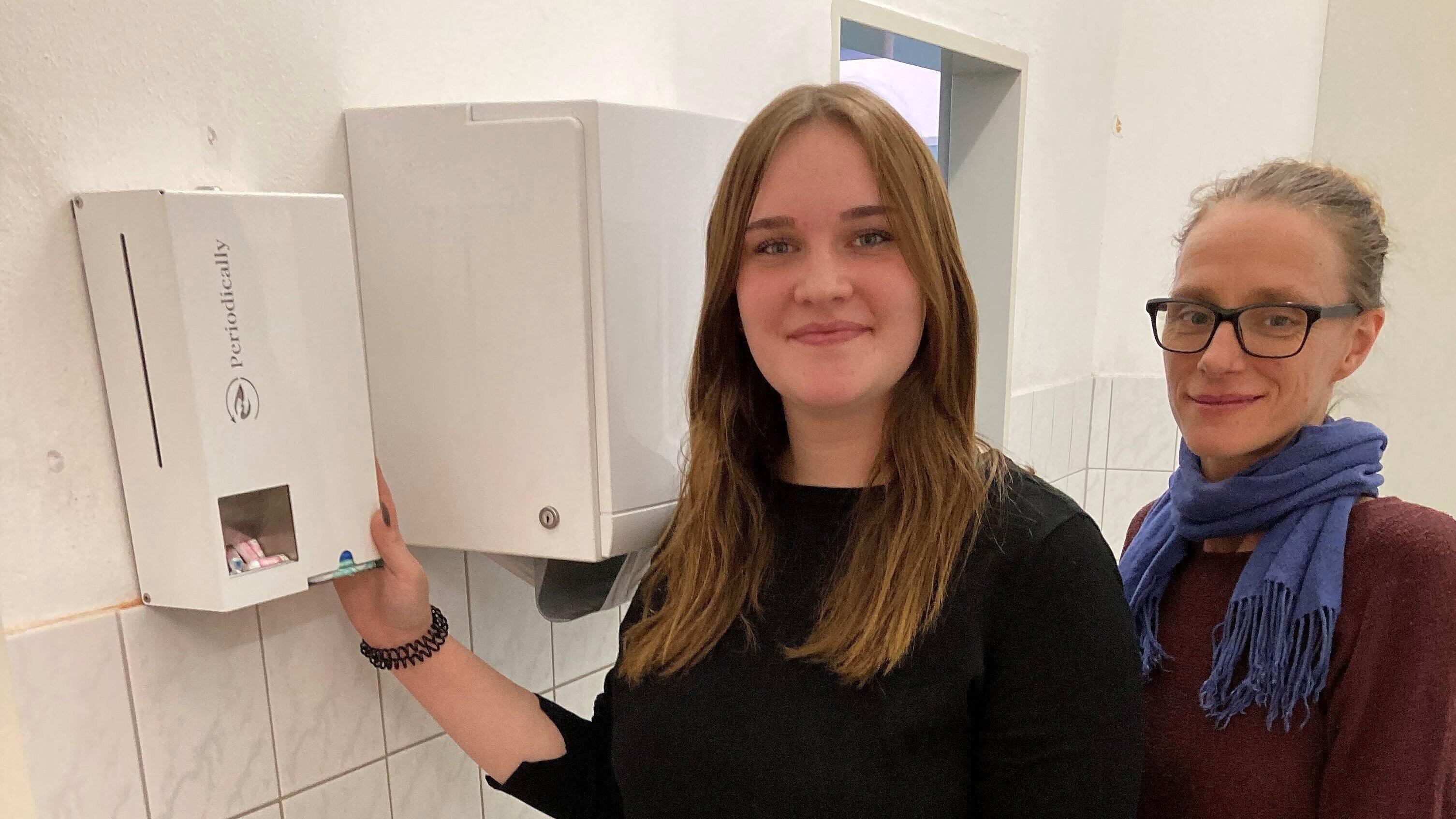 Bereits seit Anfang 2023 befindet sich in der Regelschule „Die Vierte“ ein Spender für Hygieneartikel in der Mädchentoilette. Schülersprecherin Fenya Helbing (l.) hatte dies initiiert über Spenden und in Zusammenarbeit mit Schulsozialarbeiterin Nadja Müller (r.) sowie der Schulleitung und mit weiteren Helfenden auch umgesetzt. Jetzt beteiligt sich „Die Vierte“ auch am weiteren Test und Erfahrungsammeln über das Zukunftspaket. . © Stadt Gera / Catrin Heinrich