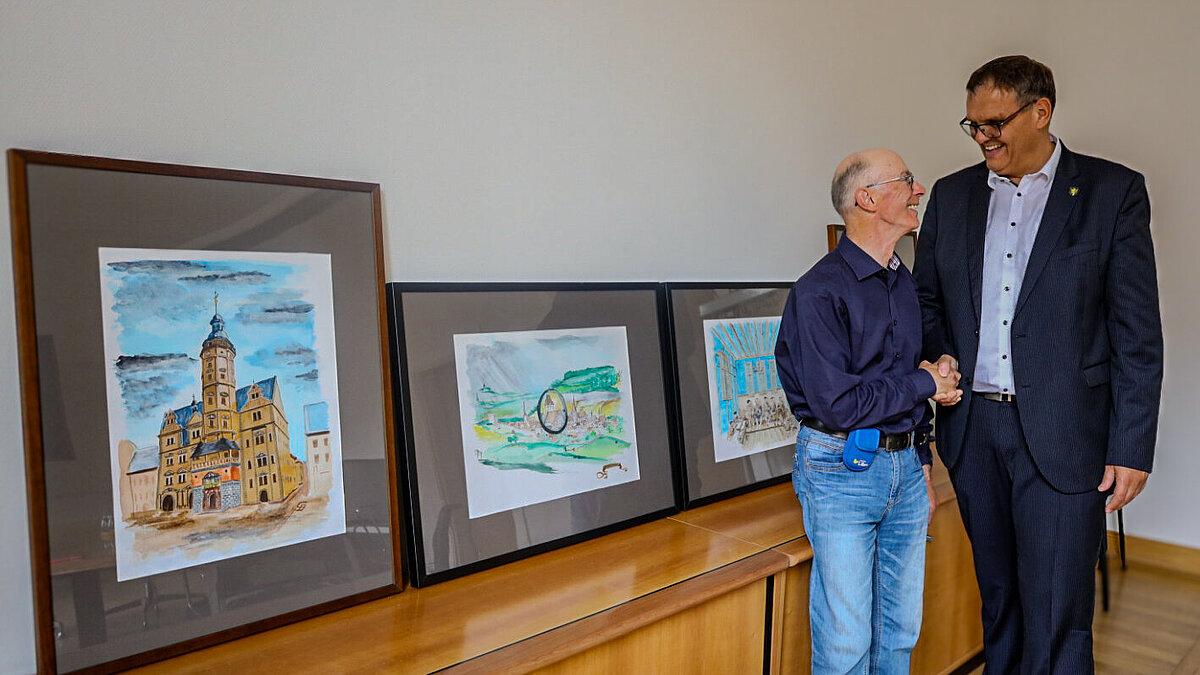 Oberbürgermeister Kurt Dannenberg und Künstler Günter Domkowsky schütteln Hände vor Bildern. © Stadt Gera
