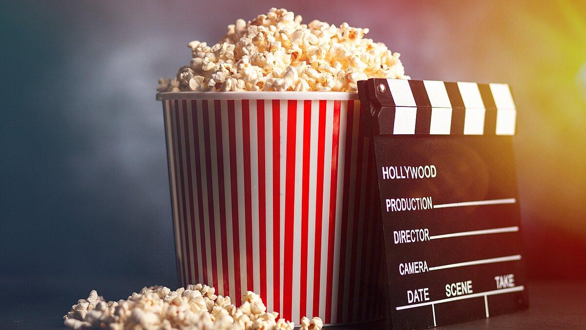 Eine Filmklappe lehnt an einer Tüte Popcorn