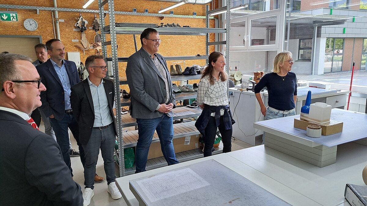 Mehrere Menschen in einer Produktionshalle für orthopädische Schuhe, Metallregale im Hintergrund, vorn ein großer Zuschneidetisch. © Stadt Gera