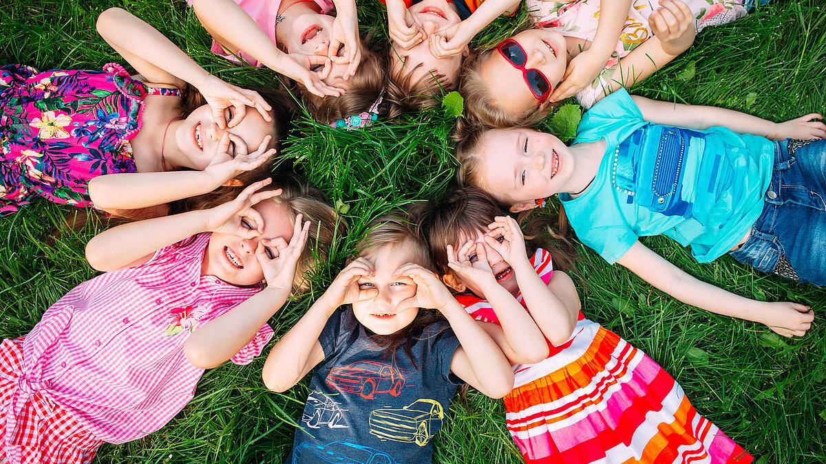 Kinder liegen auf der Wiese und schauen in den Himmel. © Adobe Stock