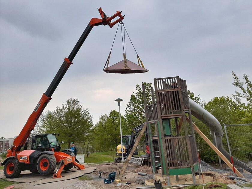Mit Hilfe eines Krans wird der neue Rutschenturm auf dem Spielplatz aufgestellt