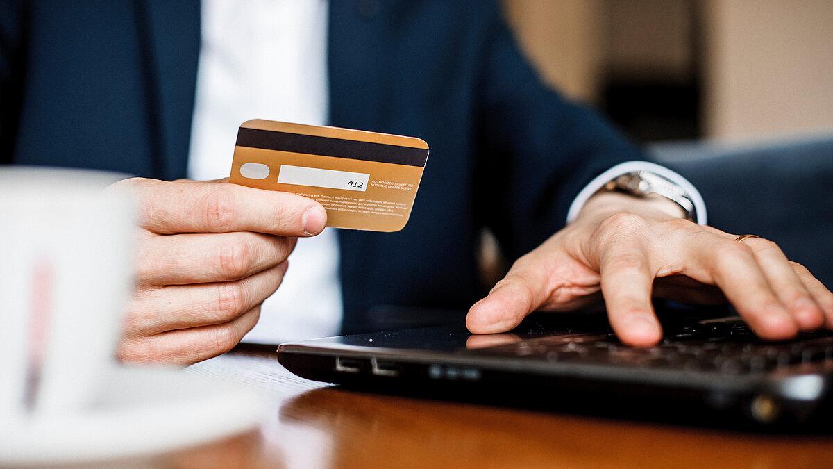Mann hält eine Kreditkarte in der Hand und tippt auf einem Laptop