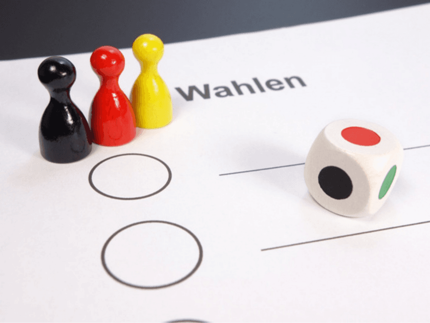 Zettel mit der Überschrift Wahlen, drei (schwarz, rot, gelb) Spielfiguren aneinandergereiht und ein weißer Würfel mit farbigen Kreisen (schwarz, rot, grün). © von blickpixel über Pixabay