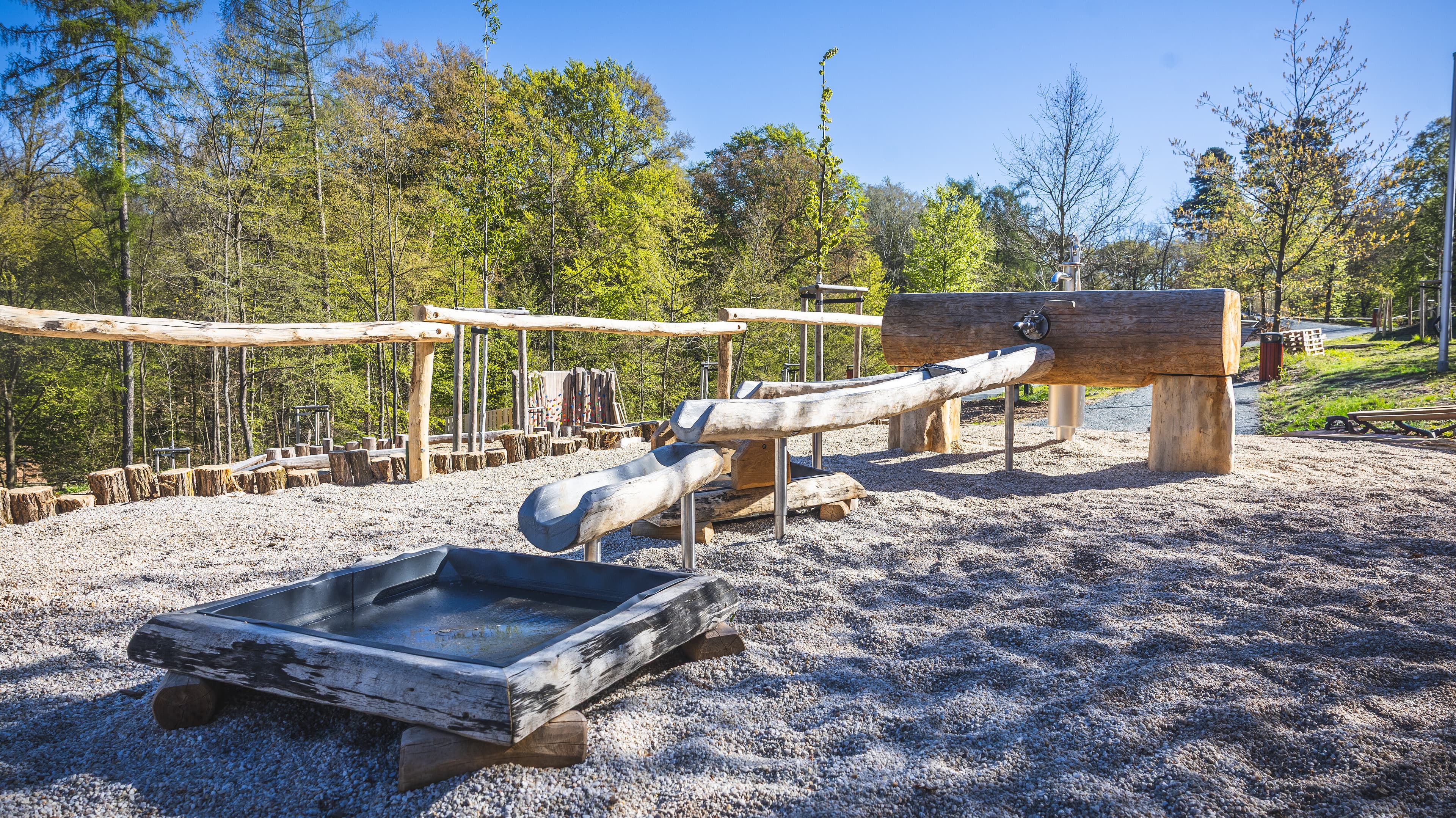 Ein hölzerner Wasserspielplatz mit Pumpe, im Hintergrund grün. © Stadt Gera