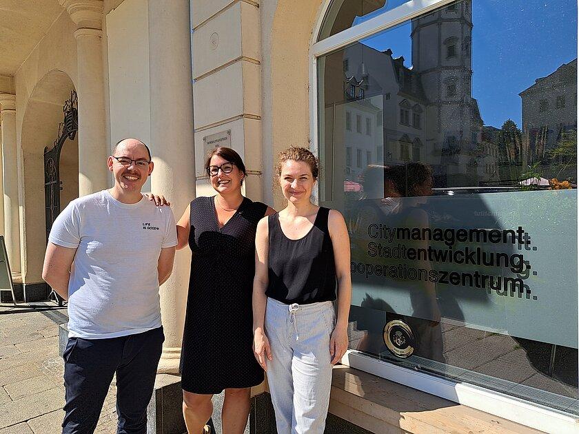 Zwei Frauen und ein Mann, die vor einem Bürofenster auf dem Markt stehen. © Stadt Gera