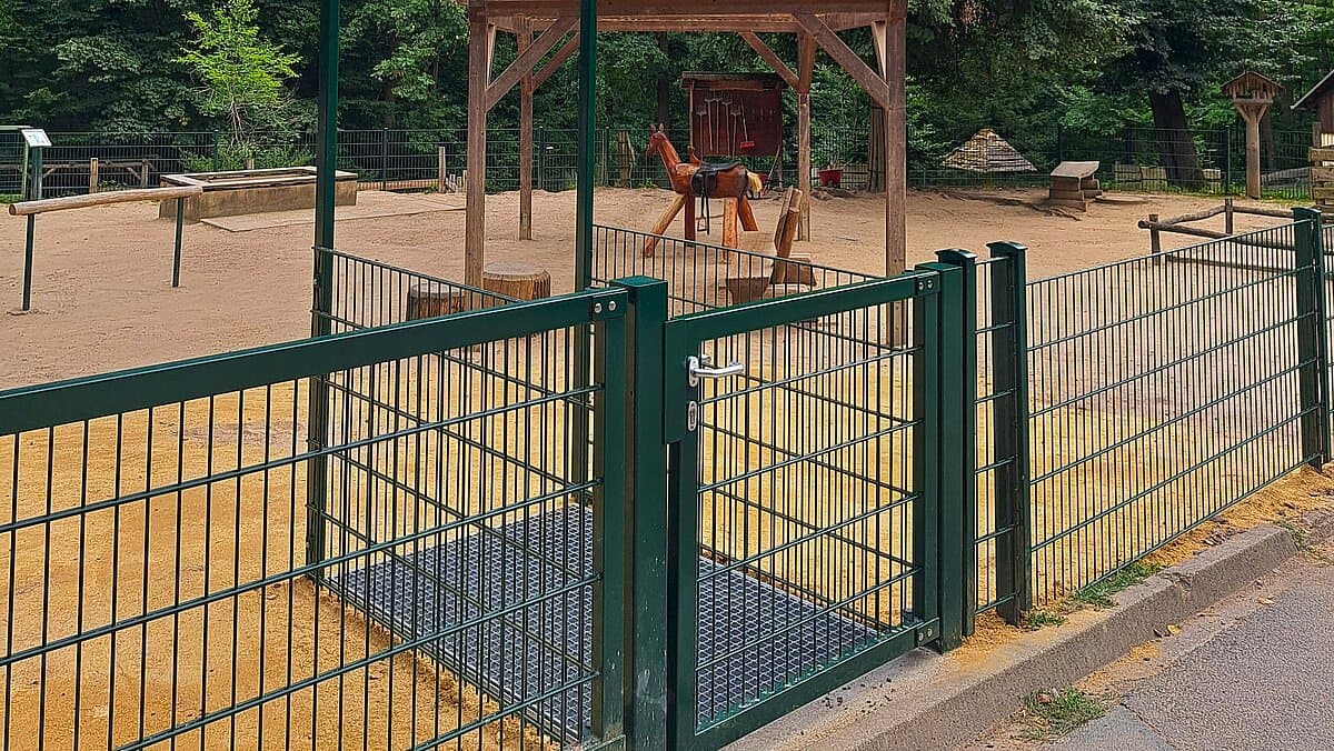 Ein grünes Metalltor samt Zaun, hinter dem ein Sandplatz für die Tiere liegt. © Stadt Gera