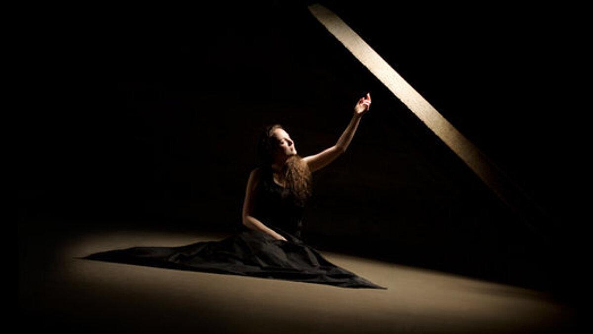 Abschlussarbeit von Sophia Hehemann, Auszubildende der SBBS Wirtschaft und Verwaltung Gera, zu sehen ist eine in schwarz gekleidete Frau die in der Dunkelheit sitzt und nur von einer kleinen Lichtquelle über ihr, angeleuchtet wird. Ihre linke Hand hält sie gegen das Licht.. © Sophie Hehemann