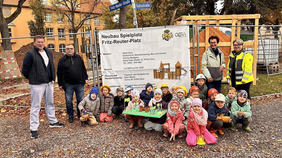 Eine Kindergruppe und mehrere Erwachsene vor der Bautafel, die den künftigen Spielplatz zeigt. © Kita Zwötzener Spatzennest