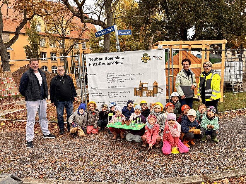 Eine Kindergruppe und mehrere Erwachsene vor der Bautafel, die den künftigen Spielplatz zeigt. © Kita Zwötzener Spatzennest