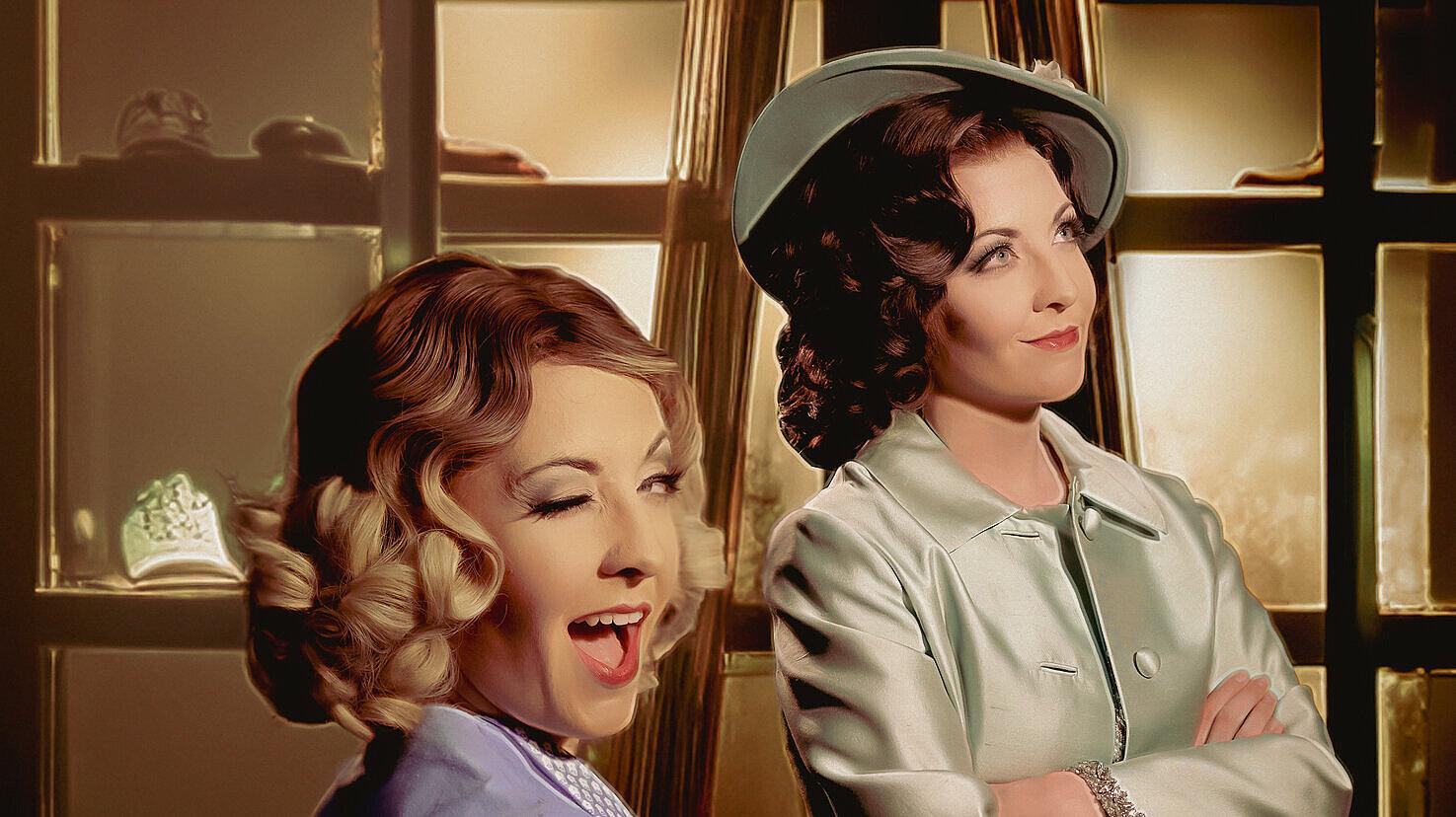 Zwei weibliche Schauspielerinnen während einer Aufführung - eine lächelt und blinzelt in die Kamera. © Theater Gera Altenburg